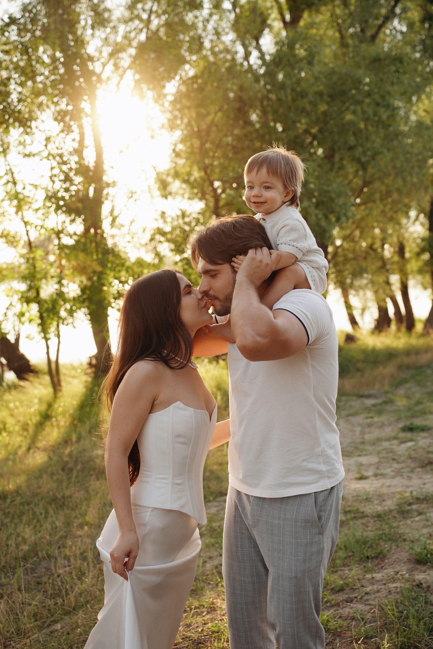 Сімейна фотосесія на природі у Києві - батьки цілуються, дитина сидить на плечах у батька